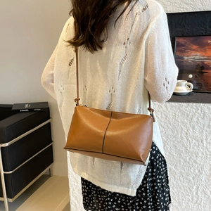 Minimalist brown leather shoulder bag shown on a model wearing white knitwear