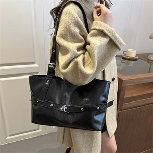 Elegant black leather tote bag with adjustable buckle strap shown on model's shoulder
