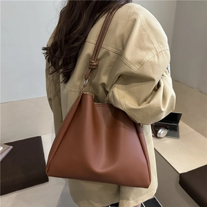 Brown soft PU leather bucket tote bag with knot shoulder strap worn by a model