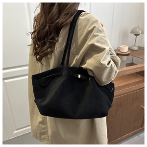 Minimalist black tote bag with metal buckle shown as styled on a woman's shoulder