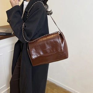 Dark brown oil wax leather shoulder bag with metal chain strap shown on model's side