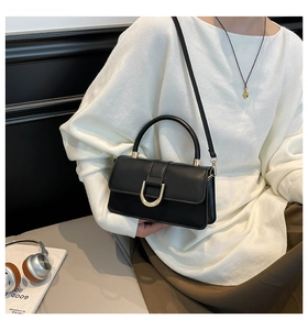 Close-up of black leather handbag featuring a stylish gold D-buckle and sleek handle