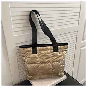 Detailed view of the gold quilted tote bag with black woven straps and puffer fabric texture