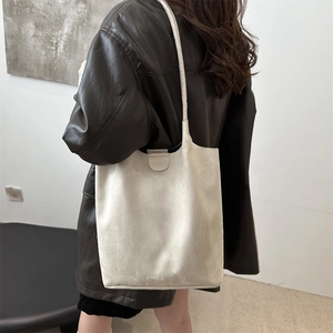 Minimalist beige suede tote bag with slim shoulder strap worn on a leather jacket