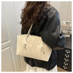 Detail of cream white tote bag featuring unique knot-style shoulder strap and embossed logo
