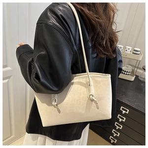 Detailed side view of off-white leather tote bag with knotted shoulder strap and embossed text