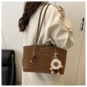 Detail of brown suede tote bag with leopard texture and plush sheep charm on shoulder