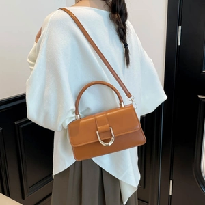 Brown rectangular handbag with golden U-shaped buckle shown on model in a modern room