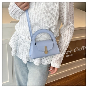 Detail of light blue crossbody bag with gold metal clasp and curved top handle