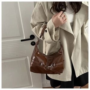 Detail of dark brown glossy hobo bag with silver buckle worn with a beige trench coat