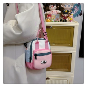 Crossbody view of a colorful patchwork canvas bag worn over a beige coat with pink strap