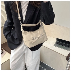 Vue détaillée du sac bandoulière crème en similicuir porté avec un blazer rayé élégant
