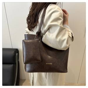 Deep brown vintage tote bag with small pouch shown on shoulder in a minimalist setting