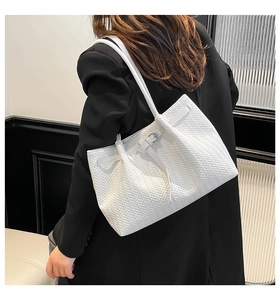 Detailed view of white woven texture tote bag worn by a model in a black blazer