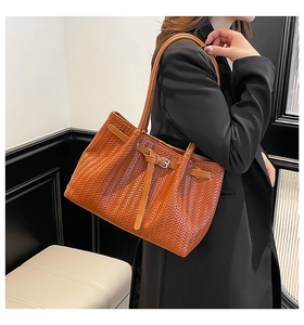 Detail of a deep brown woven tote bag featuring a leather strap with a metal buckle clasp