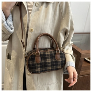 Detailed close-up of a vintage plaid bowling bag with brown leather handles and gold hardware