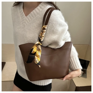 Close-up of brown leather tote bag with a decorative floral silk scarf on the handle
