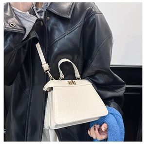 Detalle de bolso crema con textura de cocodrilo y cierre giratorio dorado sobre abrigo