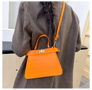 Detail der leuchtend orangen Handtasche mit Krokoprägung, goldenem Drehverschluss und Griff