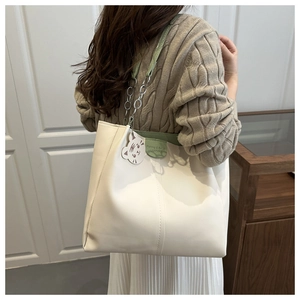 Detail of white tote bag with green leather straps, metal chain, and cute tiger charm