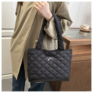 Close-up of black quilted tote bag with silver bow detail and thick padded shoulder strap