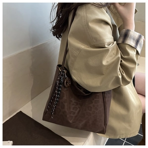 Detail view of large leopard print tote bag with woven charm on a stylish trench coat