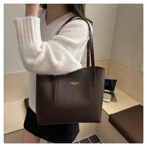 Close-up of a large dark brown leather tote bag worn by a model in a cozy office setting