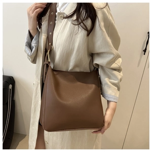 Brown leather bucket bag detail with adjustable metal eyelet strap for shoulder carry