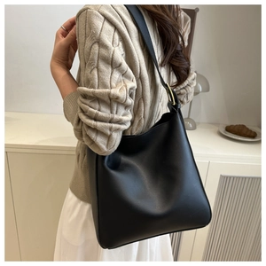 Minimalist black matte leather bucket bag with gold buckle shown on shoulder