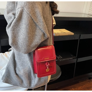 Détail du petit sac en cuir verni rouge avec lettrage doré et pendentif métallique