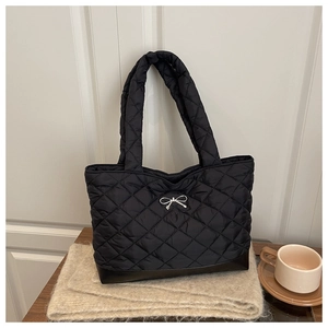 Detail of black quilted tote bag with silver bow accent and reinforced leather base
