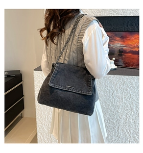Detail of dark denim crossbody bag with metal chain strap worn in a modern interior