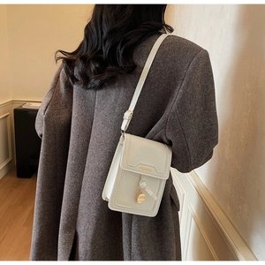 Vue détaillée d'un petit sac à bandoulière blanc cassé avec texte doré et pendentif