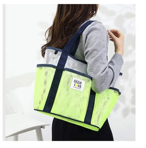 Detail view of large mesh tote bag in neon yellow and white worn on a shoulder
