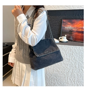 Detail of dark grey denim shoulder bag with metal chain strap worn by a female model