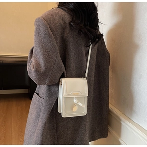 Gros plan d'un sac à bandoulière en cuir blanc avec pendentif doré sur un mannequin