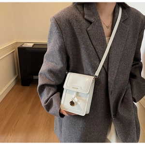 Détail du petit sac bandoulière blanc avec logo FASHION et pendentif métallique