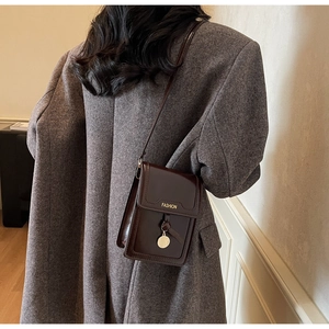 Détail d'un petit sac bandoulière en cuir marron foncé avec pendentif doré sur manteau