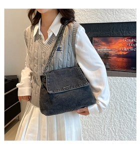 Detail of grey denim crossbody bag with metal chain strap worn by a model in casual setting
