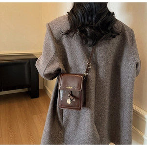 Détail d'un petit sac bandoulière en cuir verni marron foncé porté sur une veste grise