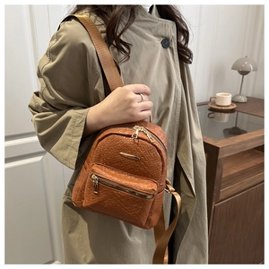 Detailed view of brown woven PU leather backpack with gold zippers and metal logo plate
