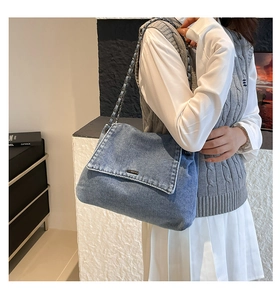 Detail of blue denim flap bag with metal chain strap worn by a model in casual setting
