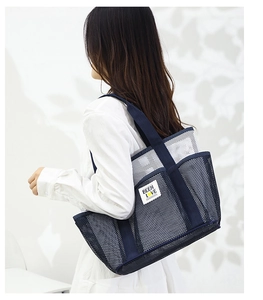 Detail of navy blue mesh beach tote bag with brand label worn by model on white background