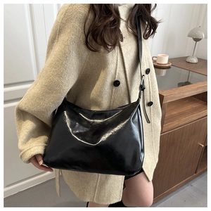 Détail du sac hobo en similicuir noir brillant avec bandoulière réglable sur manteau