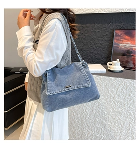 Detail of blue denim shoulder bag showing metal chain strap and stitching on a female model