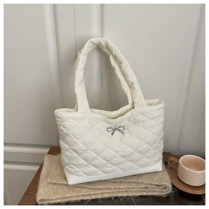 Close-up of ivory quilted tote bag featuring a silver metal bow and textured stitching