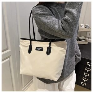 Detail of trendy off-white tote bag with black straps and central brand logo patch