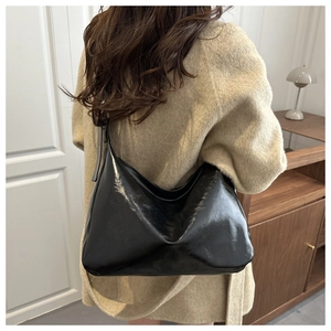 Vue latérale d'un grand sac hobo noir brillant porté sur un manteau beige dans un intérieur