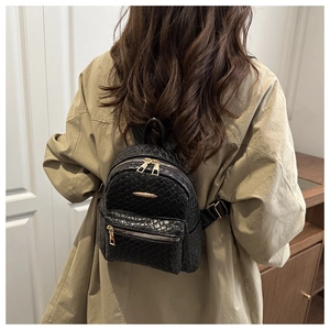 Mini sac à dos noir en cuir tressé avec zips dorés sur un trench-coat de couleur kaki