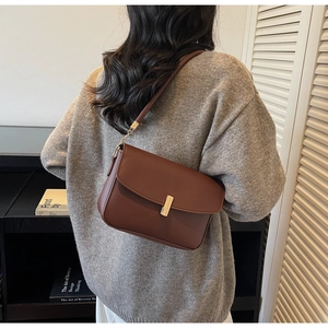Detail of dark brown leather crossbody bag with gold buckle on a gray sweater